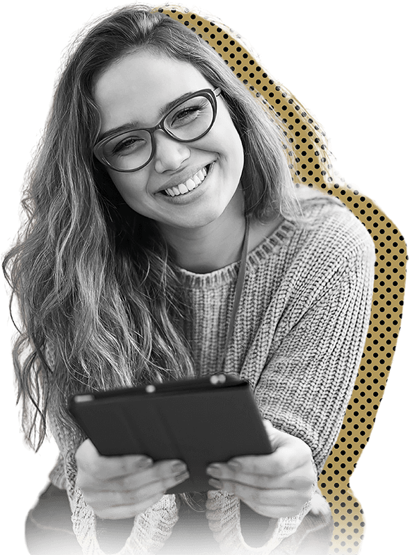 A woman in a sweater and glasses smiles while holding a tablet, showcasing a warm and inviting expression